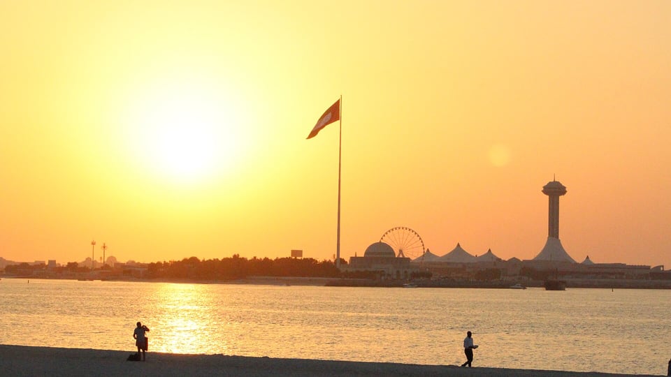 Sunset over the water from Corniche Beach, with a flagpole and the Marina Mall tower on the horizon
