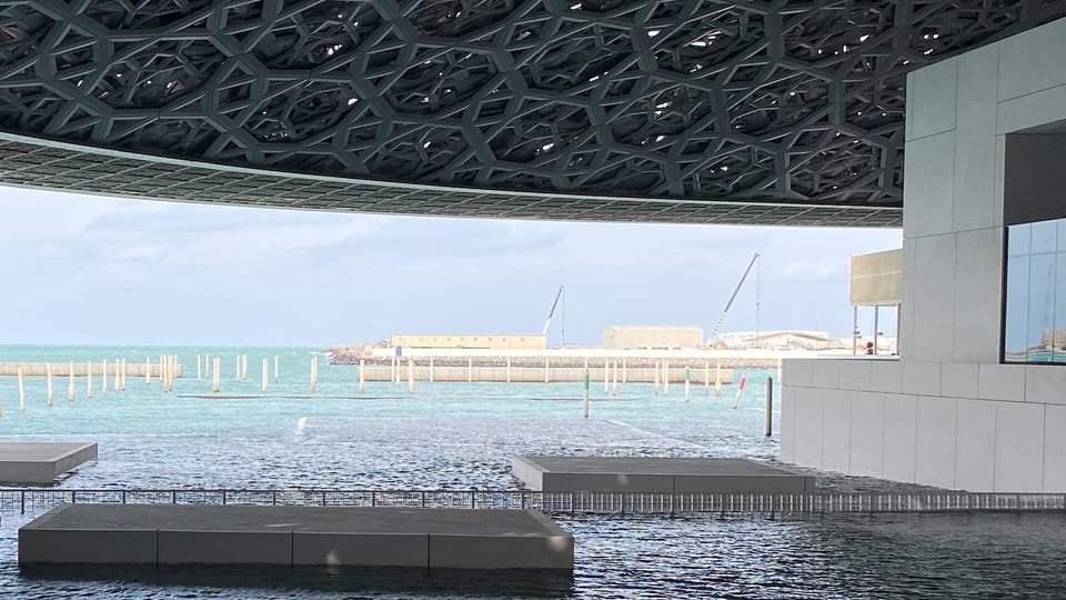 The perforated dome of Louvre Abu Dhabi over open water and a white gallery building