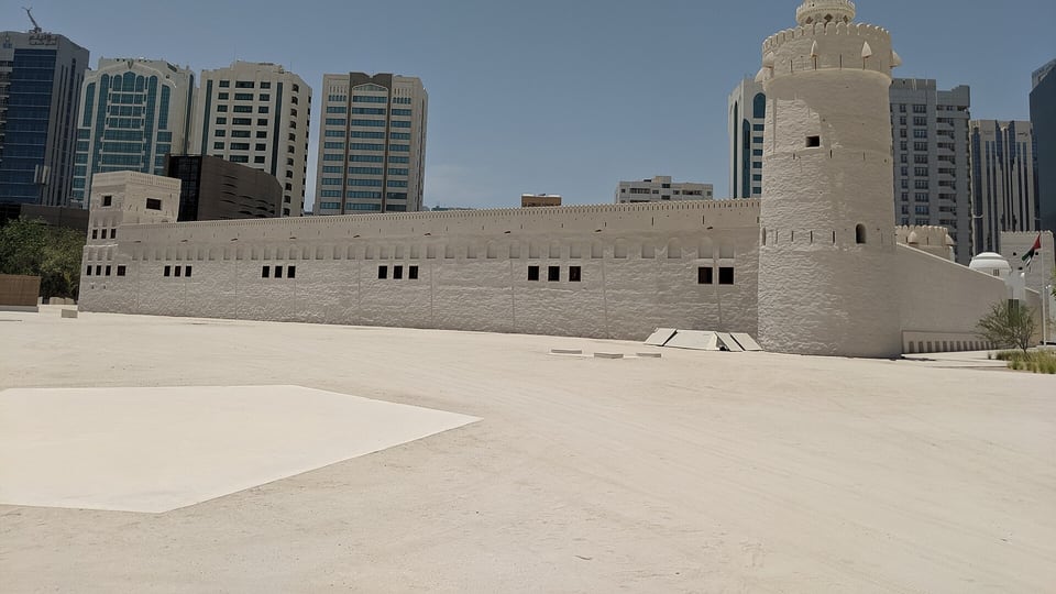 The white walls and round corner tower of Qasr Al Hosn with towers rising behind