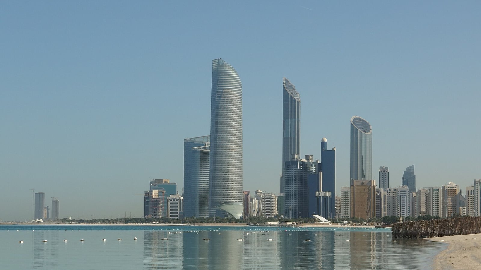 Abu Dhabi’s waterfront towers reflected in the shallow water beside Corniche Beach