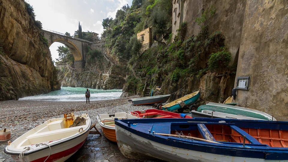Small boats on the pebble beach of the Furore fjord, under the arched road bridge