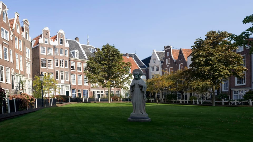 Historic gabled houses around the lawn of the Begijnhof courtyard in Amsterdam, with a statue in the foreground