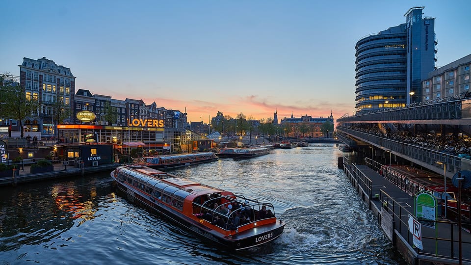 A glass-roofed canal cruise boat setting off from its landing stage in central Amsterdam at dusk