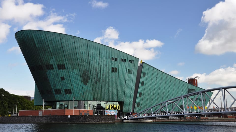 The green copper-clad NEMO Science Museum building rising above the water beside a bridge in Amsterdam