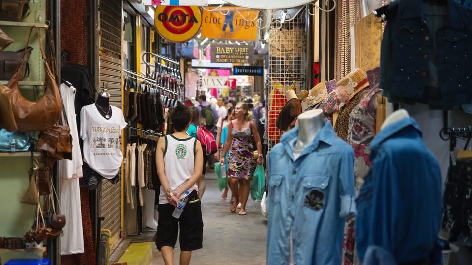 Shoppers walking a narrow clothing lane at Chatuchak Weekend Market in Bangkok