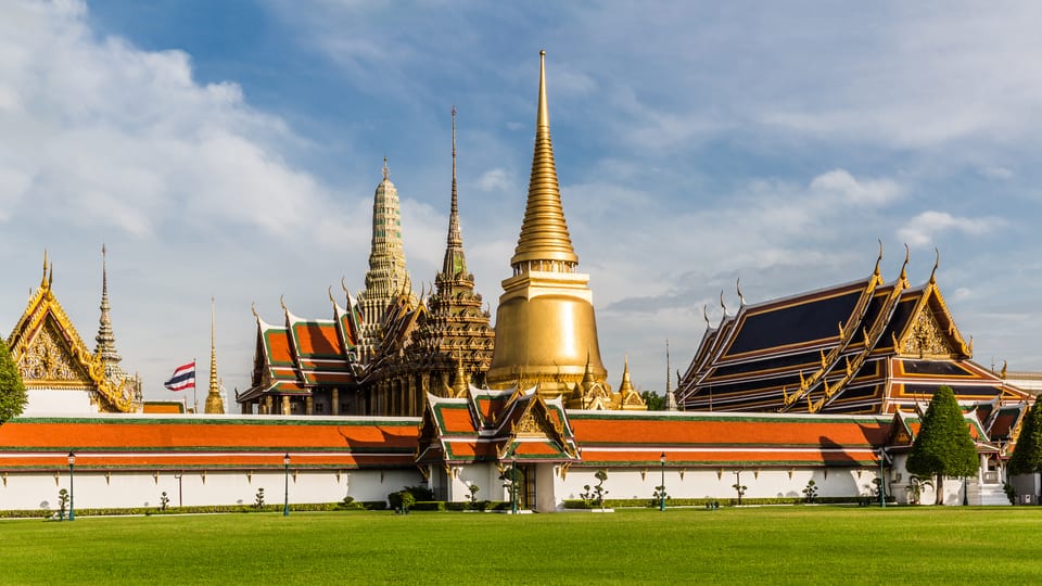 The golden chedi and spires of Wat Phra Kaew rising behind the white walls of the Grand Palace in Bangkok