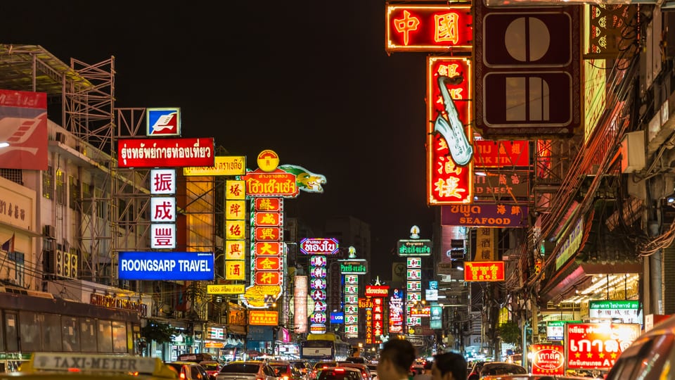 Neon shop signs above traffic on Yaowarat Road in Bangkok's Chinatown at night