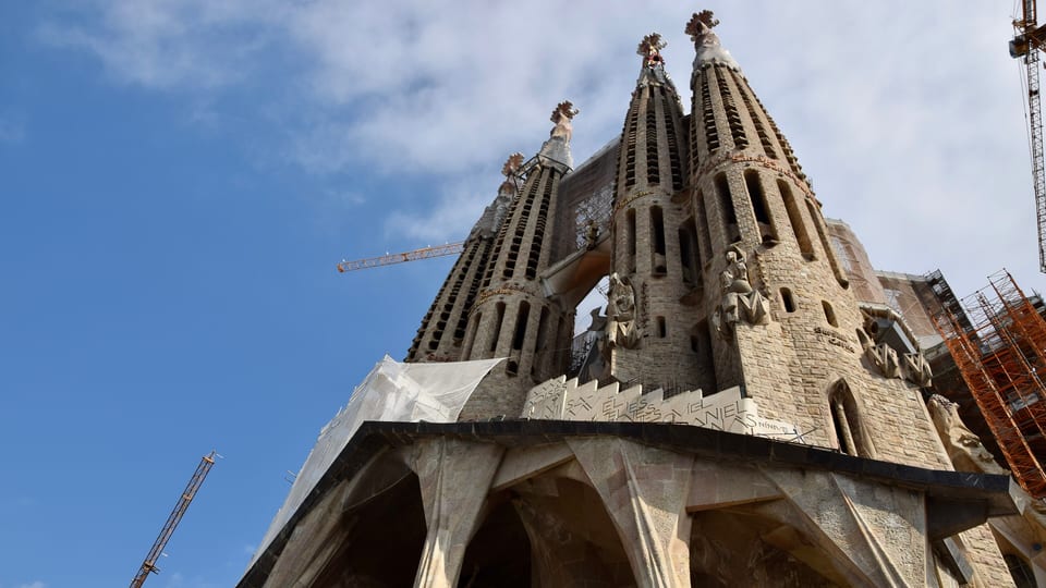 Towers above the Passion facade of the Sagrada Família basilica in Barcelona against a blue sky