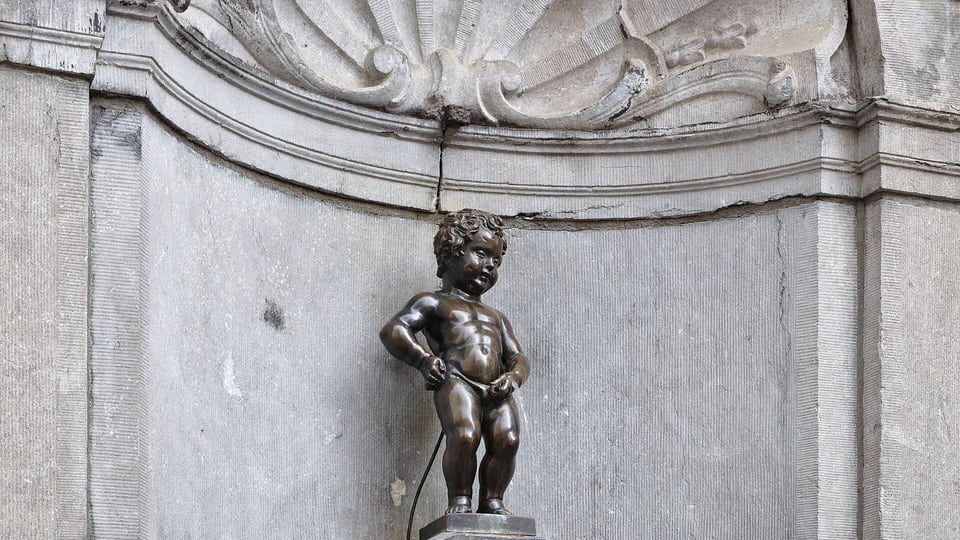 The small bronze Manneken Pis fountain statue in its stone niche near the Grand-Place