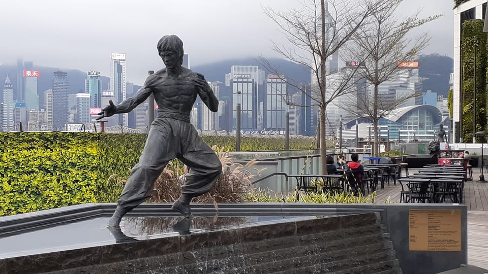 The Bruce Lee statue on the Avenue of Stars with the Hong Kong Island skyline across Victoria Harbour