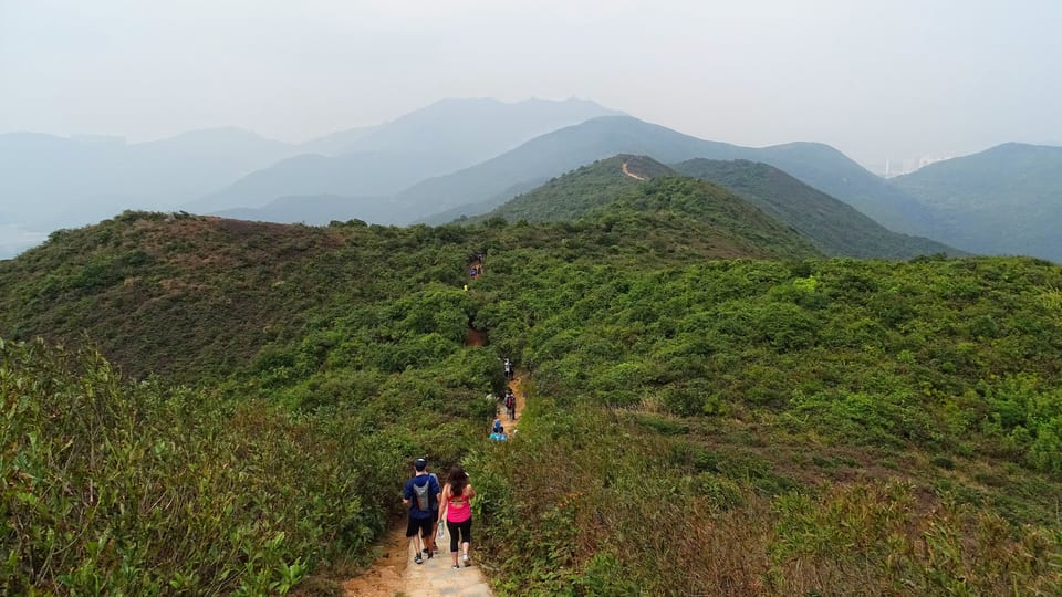 Hikers on the Dragon's Back ridge trail in Shek O Country Park looking north over green hills