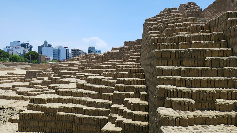 Stepped adobe walls of the Huaca Pucllana pyramid with Miraflores apartment blocks behind