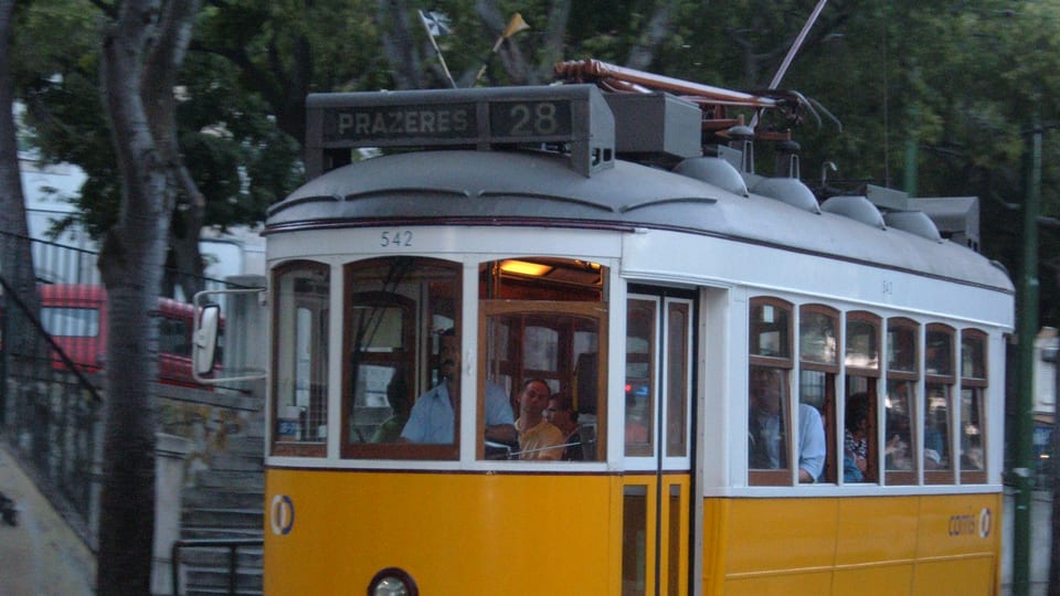 A yellow line 28 tram signed Prazeres about to descend Rua da Voz do Operário in Lisbon