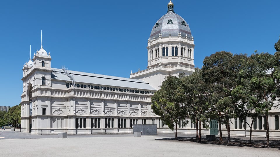 The domed Royal Exhibition Building beside Carlton Gardens under a blue sky