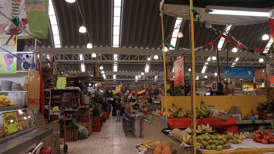 Fruit and juice stalls along a covered aisle in the Mercado de Medellín in Roma