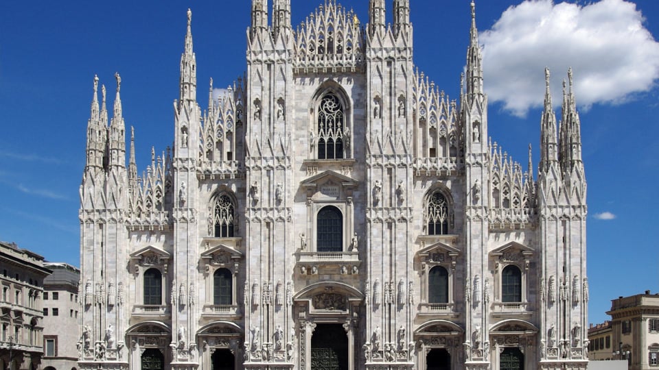 The white marble facade and pinnacles of Milan Cathedral, the Duomo, under a clear blue sky