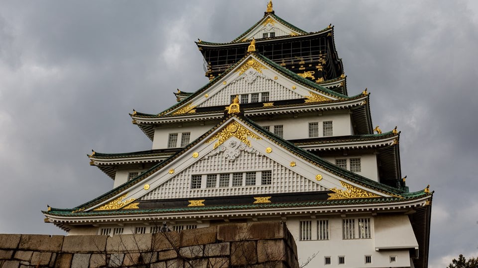 The white and green main tower of Osaka Castle rising above stone walls