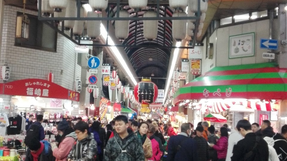 A crowded covered aisle and food stalls inside Kuromon Market in Osaka