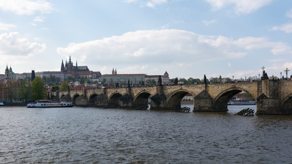 The stone arches of Charles Bridge across the Vltava in Prague, with Prague Castle on the skyline behind