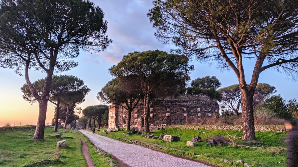 The ancient paved Via Appia Antica lined with umbrella pines and ruins at sunset outside Rome