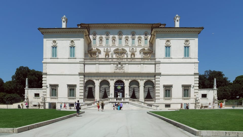 The white facade of the Galleria Borghese villa in Rome, approached by a path between lawns