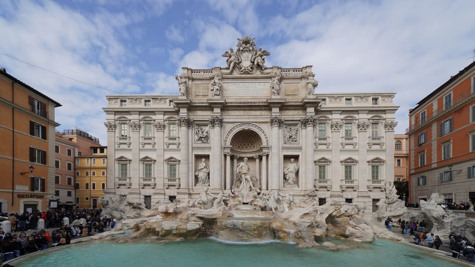 The Trevi Fountain in Rome with its sculpted facade and turquoise basin, and visitors around the edge