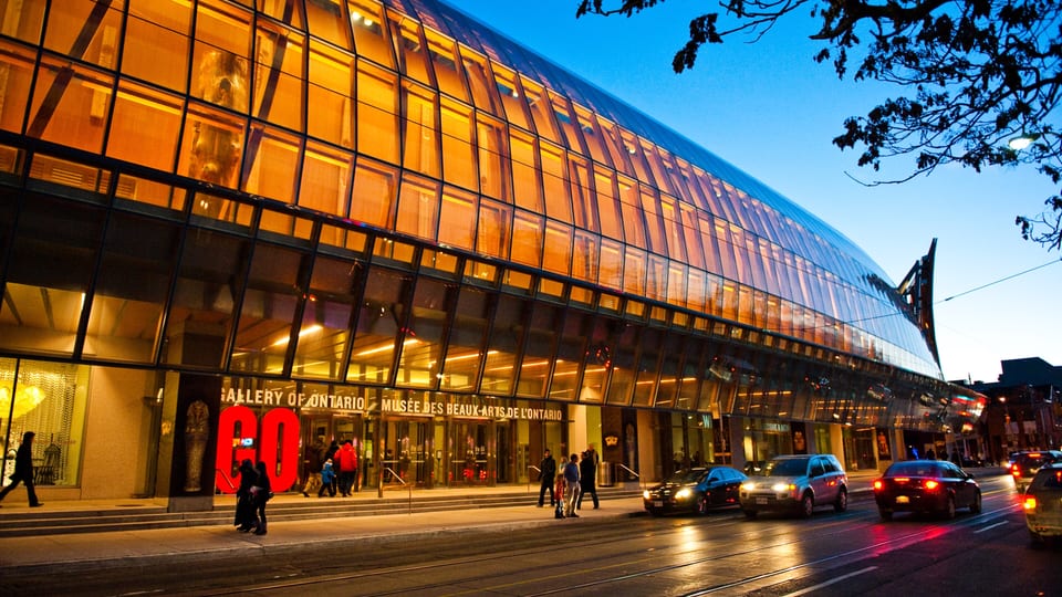 The curved glass and timber Frank Gehry facade of the Art Gallery of Ontario lit at dusk on Dundas Street West