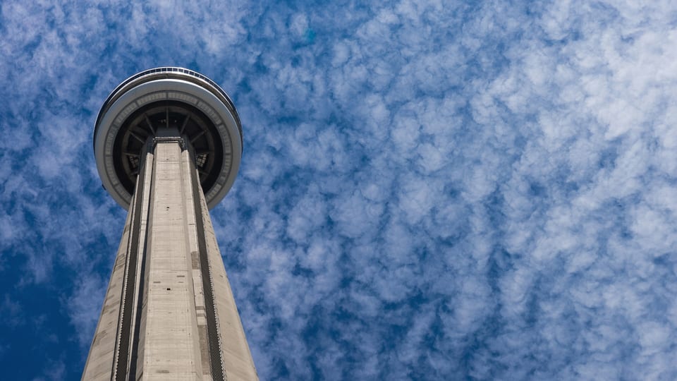 Looking up the concrete shaft of the CN Tower to its main pod against a cloud-dappled sky