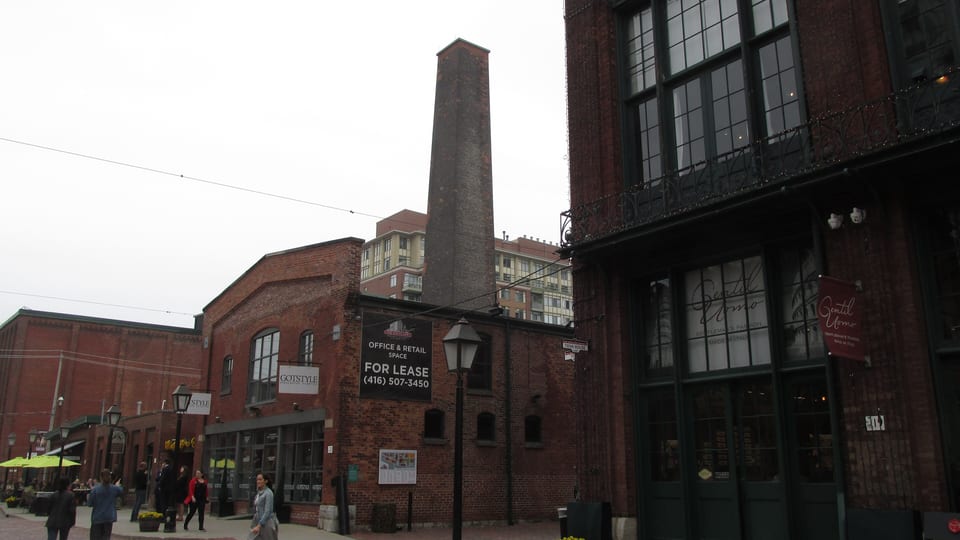 Victorian red-brick industrial buildings and a tall chimney along a pedestrian lane in the Distillery District