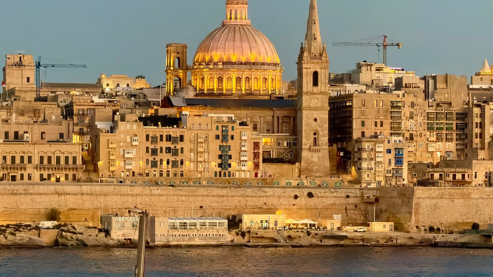 The dome of the Carmelite church and the spire of St Paul’s Anglican cathedral above the Valletta waterfront at blue hour, seen from Sliema